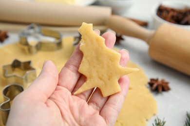 Woman holding unbaked Christmas tree shaped cookie at table, closeup