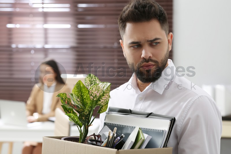 Upset dismissed man carrying box with personal stuff in office