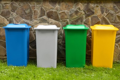 Photo of Many colorful recycling bins near stone fence outdoors