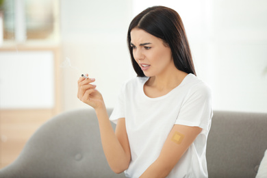 Emotional young woman with nicotine patch and cigarette at home