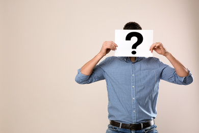 Man holding paper with question mark on grey background, space for text