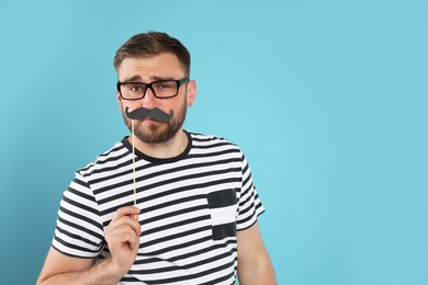 Photo of Funny man with fake mustache on turquoise background, space for text