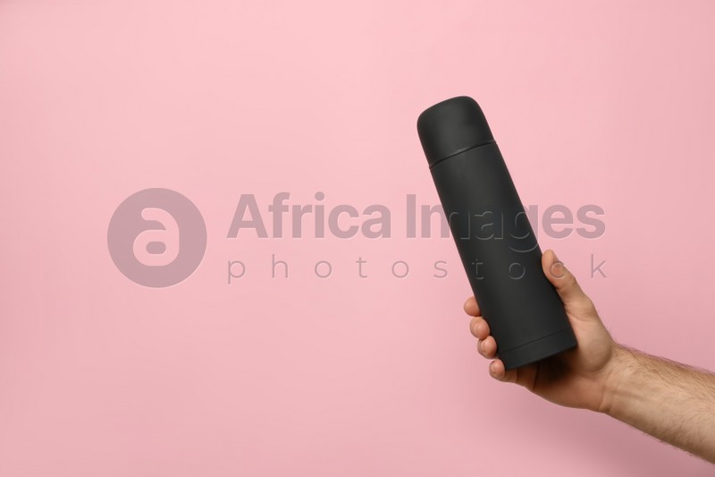 Man holding black thermos on pink background, closeup. Space for text