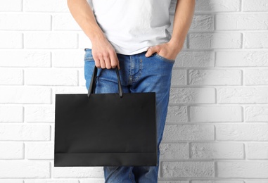 Man holding mock-up of paper shopping bag against wall