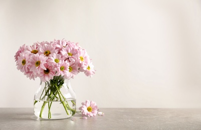 Vase with beautiful chamomile flowers on table against light background. Space for text