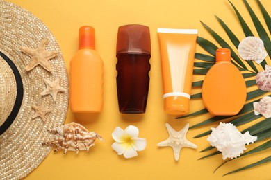 Sun protection products, shells and beach hat on orange background, flat lay