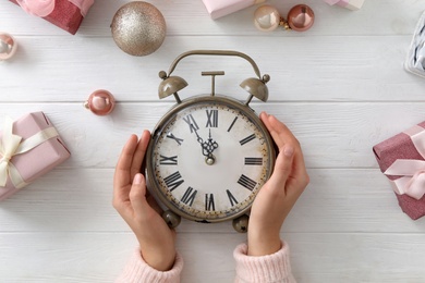 Photo of Woman with alarm clock near Christmas decor on white wooden background, top view. New Year countdown