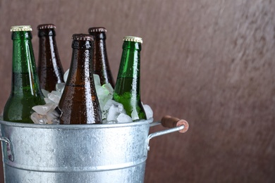 Photo of Metal bucket with bottles of beer and ice cubes on brown background, closeup. Space for text