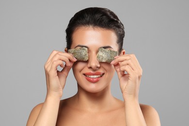 Woman covering eyes with tea bags on grey background. Skin care