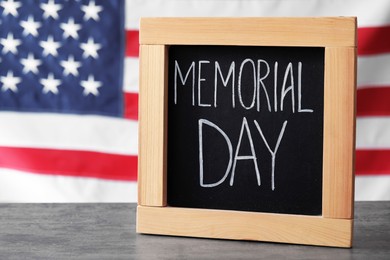 Photo of Blackboard with phrase Memorial Day on wooden table against American flag