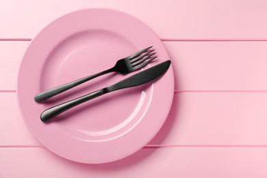 Photo of Ceramic plate with cutlery on pink wooden table, top view. Space for text