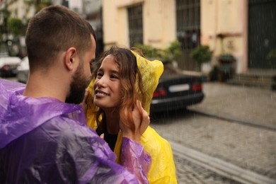 Photo of Young couple in raincoats enjoying time together on city street, space for text
