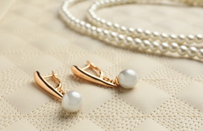 Photo of Elegant necklace and golden earrings with pearls on leather background, closeup