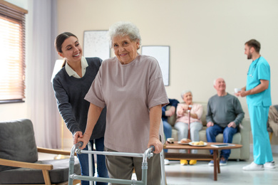Care worker helping to elderly woman with walker in geriatric hospice