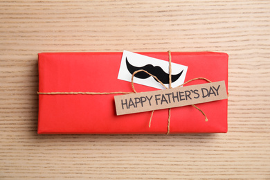 Gift box with mustache and words HAPPY FATHER'S DAY on wooden background, top view