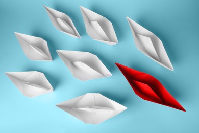 Photo of Group of paper boats following red one on light blue background, flat lay. Leadership concept