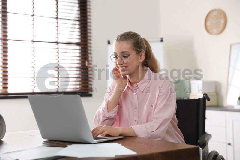 Portrait of woman in wheelchair working with laptop at table indoors