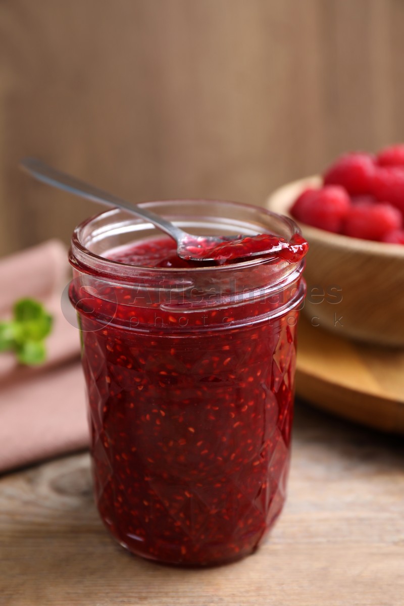 Photo of Delicious raspberry jam in jar on wooden table, closeup