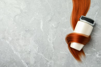 Bottle wrapped in lock of hair on light grey marble background, top view with space for text. Natural cosmetic product