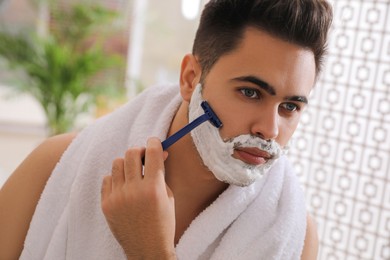 Handsome young man shaving with razor in bathroom