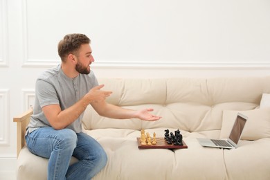 Young man playing chess with partner through online video chat at home