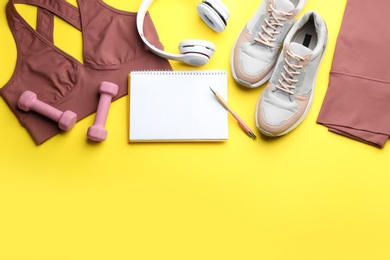 Flat lay composition with sportswear, notebook and dumbbells on yellow background, space for text. Gym workout plan