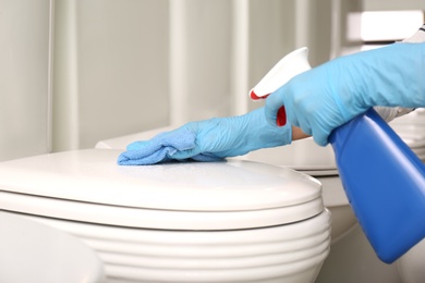 Woman cleaning toilet bowl with rag and detergent in 
store, closeup