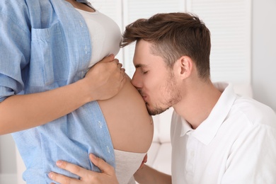 Young husband kissing his pregnant wife's tummy at home