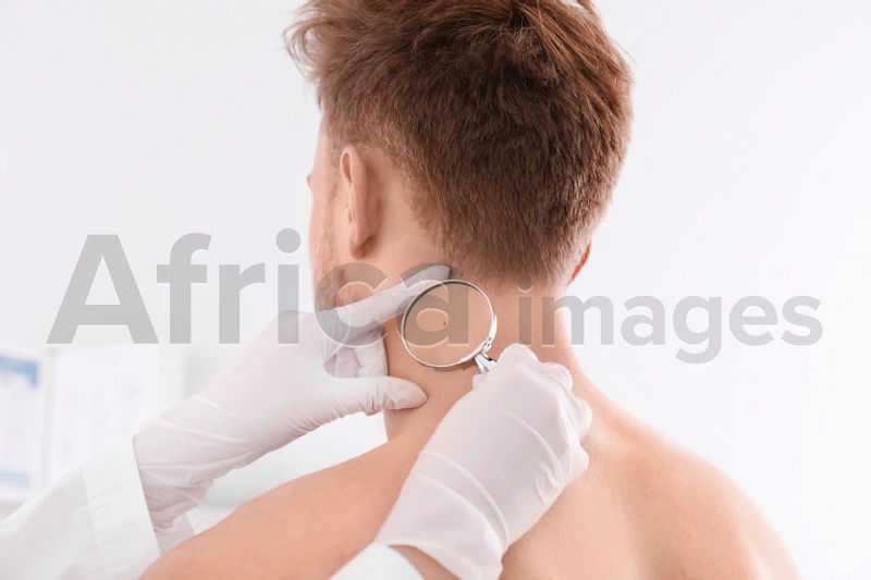 Dermatologist examining patient with magnifying glass in clinic, closeup view