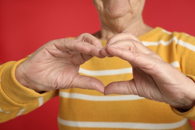 Elderly woman making heart with her hands on red background, closeup