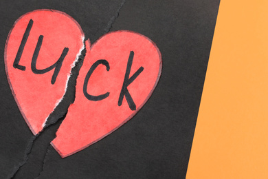 Torn heart and word LUCK written in notebook on orange background, above view