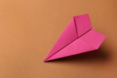 Photo of Handmade pink paper plane on brown background, space for text