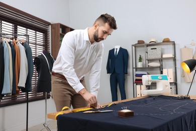 Photo of Tailor marking fabric with chalk at table in workshop