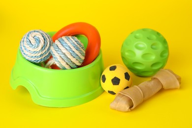 Various bright pet toys and bowl on yellow background