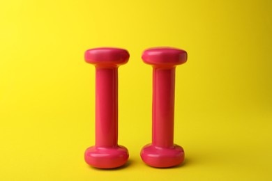 Photo of Two stylish pink dumbbells on yellow background