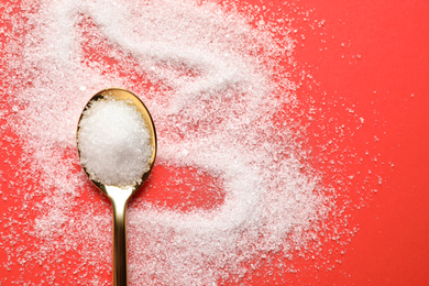 Photo of Granulated sugar and spoon on red background, flat lay