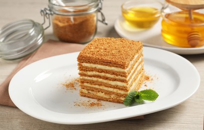 Photo of Slice of delicious layered honey cake with mint served on wooden table
