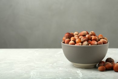 Photo of Ceramic bowl with hazelnuts on grey table, space for text. Cooking utensil