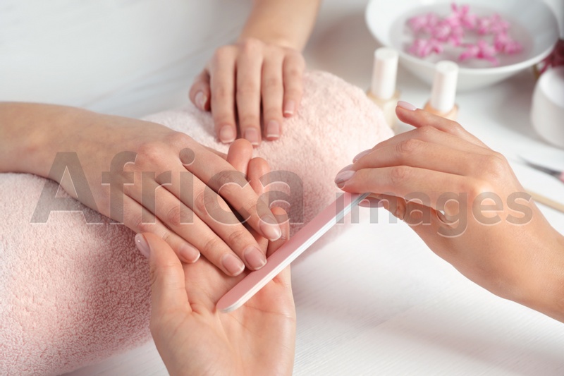 Manicurist filing client's nails at table, closeup. Spa treatment