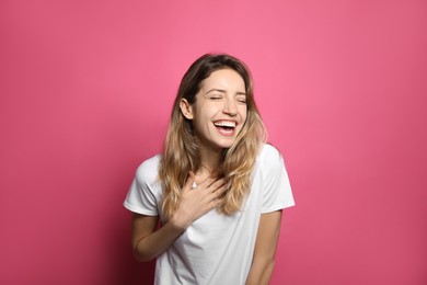 Cheerful young woman laughing on pink background
