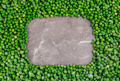 Frame made with frozen peas on brown marble table, top view. Space for text