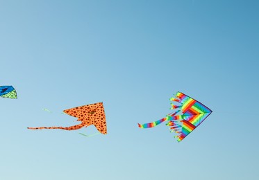 Bright rainbow kites in blue sky, low angle view