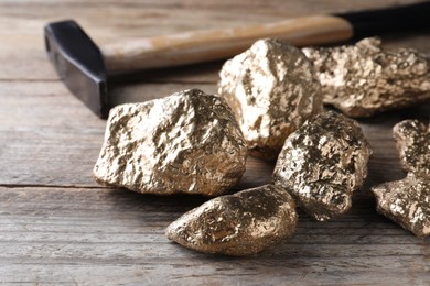 Pile of gold nuggets and hammer on wooden table, closeup