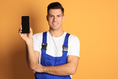 Repairman with modern smartphone on orange background