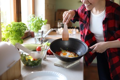 Woman holding frying pan with cooked eggs and vegetables at countertop in kitchen, closeup