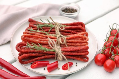 Photo of Bundles of delicious kabanosy with rosemary, peppercorn, chilli and tomatoes on white wooden table
