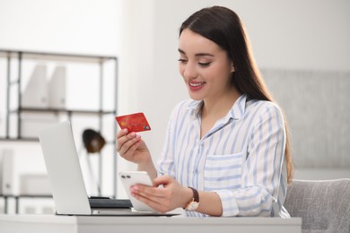 Woman with credit card using laptop and smartphone for online shopping indoors