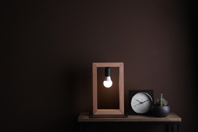 Photo of Wooden table with houseplant, alarm clock and modern lamp near brown wall in room, space for text