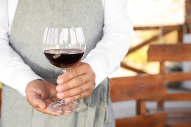 Waiter holding glass of red wine in outdoor cafe, closeup. Space for text