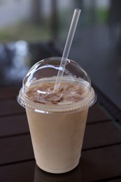 Plastic takeaway cup of delicious iced coffee on table in outdoor cafe, closeup